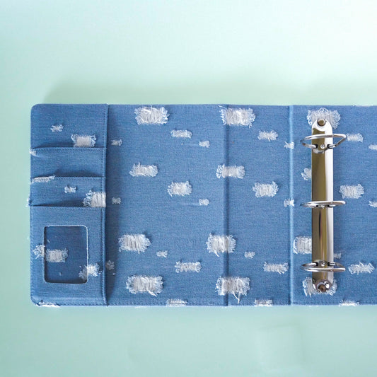 Blue fabric-bound notebook with a metal ring on a light blue background